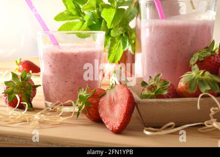 Frullato di fragola in contenitori di vetro su tavola di legno con vassoio pieno di fragole in natura primo piano. Vista frontale. Foto Stock