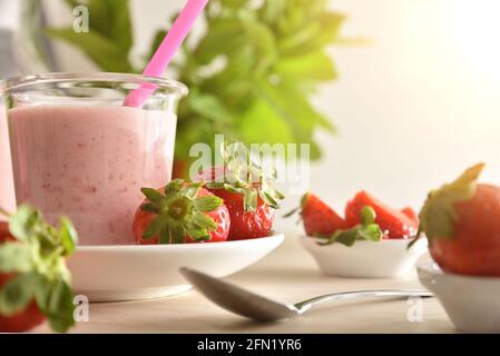 Frullato di yogurt alla fragola su tavolo di legno con ciotole piene di fragole. Vista frontale. Foto Stock