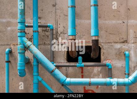 Tubi di plastica blu d'acqua sulla parete di cemento nell'edificio condominiale. Installazione di tubi di drenaggio nell'edificio. Sistema sanitario di un preservativo Foto Stock