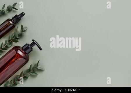 Flacone contagocce per uso medico e cosmetico, flacone dispenser scuro di gel doccia e rami di eucalipto su sfondo grigio-verde. Concetto DI SPA. In alto Foto Stock