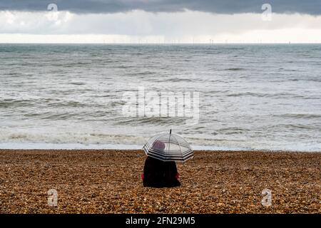 Una giovane donna che siede nella pioggia sulla spiaggia di Brighton, Brighton, Sussex orientale, Regno Unito. Foto Stock