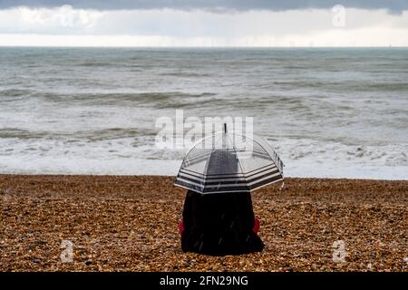 Una giovane donna che siede nella pioggia sulla spiaggia di Brighton, Brighton, Sussex orientale, Regno Unito. Foto Stock