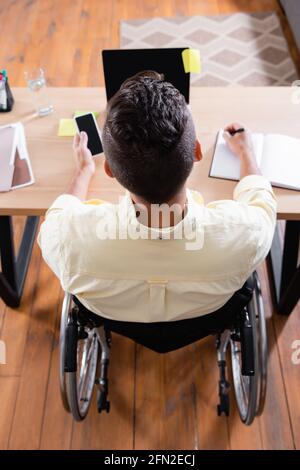 vista dall'alto della scrittura di un uomo disabile nel notebook durante il lavoro vicino al computer portatile a casa Foto Stock