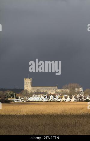 XV secolo Christchurch Priorato iluminato dal Sole contro A Dark Stormy Sky sopra le Reeds Letti di Wick Hengistbury Testa Regno Unito Foto Stock