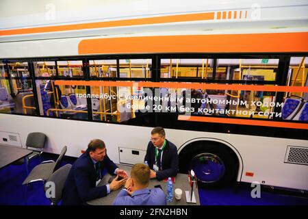 Mosca, Russia. 13 maggio 2021. I partecipanti si siedono al tavolo vicino a un autobus elettrico esposto durante la mostra internazionale ElectroTrans sul trasporto elettrico urbano a Mosca, Russia, 13 maggio 2021. La mostra durerà fino al 14 maggio. Credit: Alessandro Zemlianichenko Jr/Xinhua/Alamy Live News Foto Stock