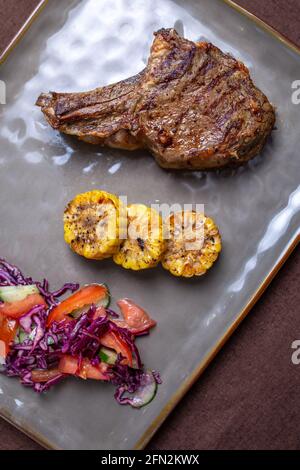 Bistecca di manzo con mais e insalata su un piatto grigio. Foto Stock