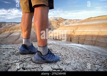 Primo piano delle gambe muscolari del giovane runner nello sport zuppe blu a siccità cracked terra rosso deserto montagne in Kazakistan Foto Stock