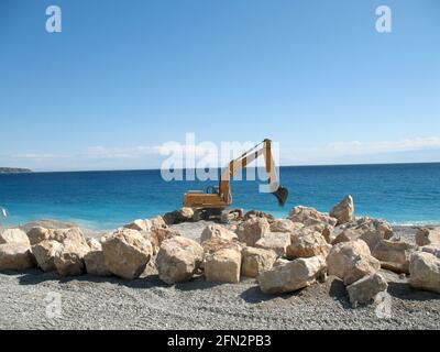 Retroescavatore giallo con braccio del pistone idraulico contro il Mar Mediterraneo Foto Stock