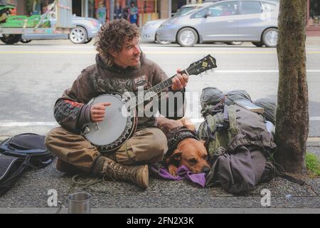 Vancouver, Canada - Aprile 25 2014: Ritratto urbano di strada di un busker uomo senza casa che gioca il banjo con il suo cane su Commercial Drive a Vancouver Est Foto Stock