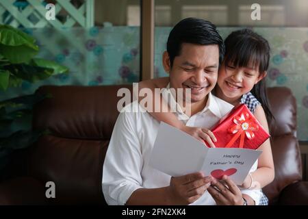 Le piccole figlie asiatiche si congratulano con papà e gli danno una cartolina E confezione regalo con sorridente e hugging.Concept di felice padre giorno Foto Stock