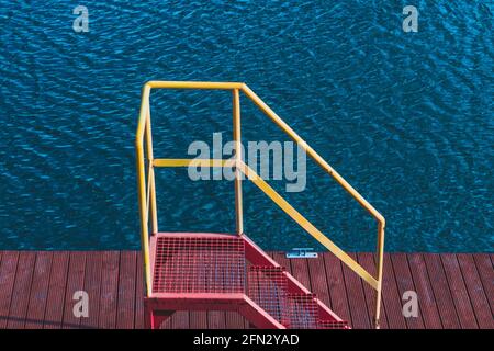 scale rosse con una ringhiera gialla che conduce al molo Foto Stock