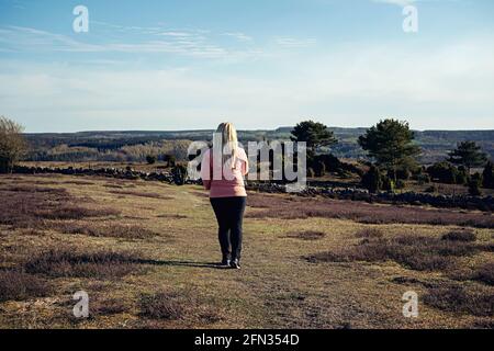 Donna con capelli biondi in giacca rosa frangivento e abbigliamento outdoor escursioni a piedi lungo i campi e bellissimo paesaggio a Brösarp, Svezia Foto Stock