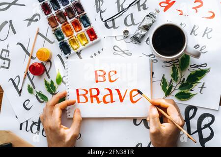 Vista dall'alto su fogli di calligraphy di mani di uomo maschio, pennini, carta, inchiostro rosso pens.craft, hobby. Lettering workshop.flat Lay motivazionale lettere parole quo Foto Stock