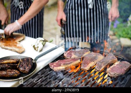 Bistecche grigliate a fiamma libera e bistecca affettabile con le mani dello chef in background Foto Stock