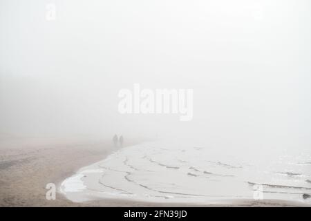 Coppia indistinta che cammina lungo la riva del mare in mistica Foto Stock