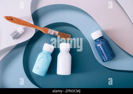 Set di vernici acriliche in taniche blu con pennello su strati colorati sfondo. Vista dall'alto Foto Stock