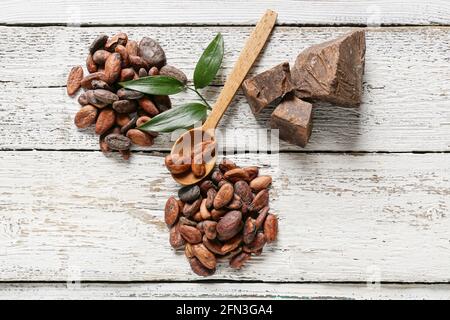 Cucchiaio con fagioli di cacao e burro su fondo di legno bianco Foto Stock