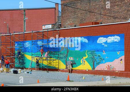 San Giovanni, NB, Canada - 30 luglio 2015: I volontari dipingono un murale sul lato di un edificio come parte del progetto dei murali e dei marigolds. Foto Stock
