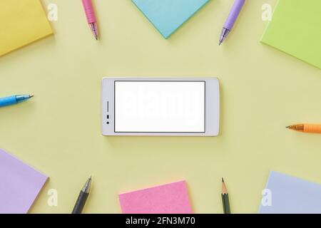 Telefono cellulare con vista dall'alto o piatto o smartphone Mock-up e Stick Note e penna su scrivania o sfondo del tavolo dell'ufficio. Forniture per ufficio su minimali gialli Foto Stock