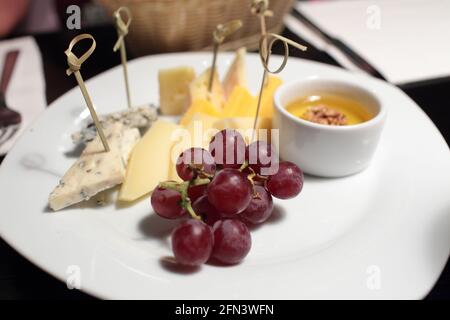 Vari formaggi a fette, uva e miele su un piatto Foto Stock