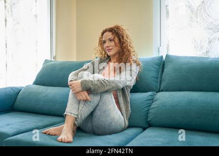 Bella donna seduta sul divano a gambe incrociate e guardando la TV. Concetto di relax a casa. Foto di alta qualità Foto Stock