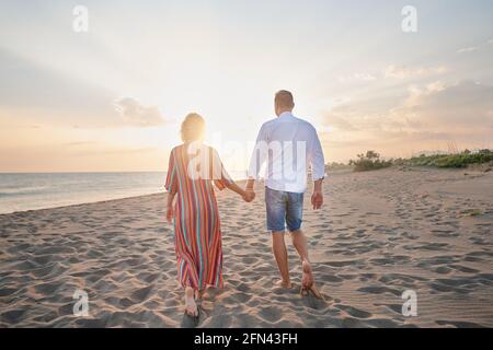 Donna e uomo che camminano insieme sulla spiaggia durante il tramonto Foto Stock