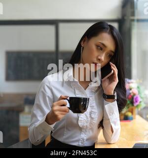 Ritratto di donna che parla al telefono mentre beve caffè in cafa Foto Stock
