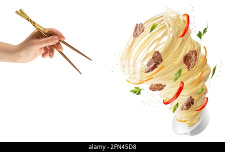 Tagliatelle con verdure e carne sotto forma di tornado. Mano con bastoni di legno e una ciotola con tagliatelle, peperoni rossi, carote, cipolle e carne. Foto Stock
