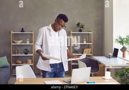 Serio uomo afroamericano che fa il lavoro di ufficio e usando il laptop nel suo ufficio domestico Foto Stock