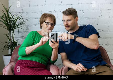 figlio insegna a sua madre di usare il telefono cellulare. donna anziana imparare ad usare le tecnologie moderne Foto Stock