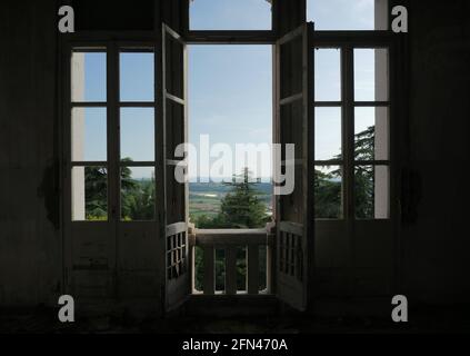 Grande finestra che si affaccia su una valle verde. Scappate da una casa abbandonata. Finestra francese rovinata dal tempo. Foto Stock