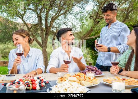 Festa tipica italiana per la vendemmia in casa di campagna. Gruppo di giovani amici riuniti a tavola con spuntini, pizza, pomodori e. Foto Stock