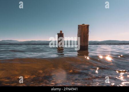 due pali di legno lavati dalle acque del lago con le montagne sullo sfondo Foto Stock