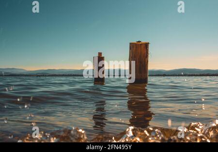 due pali di legno lavati dalle acque del lago con le montagne sullo sfondo Foto Stock