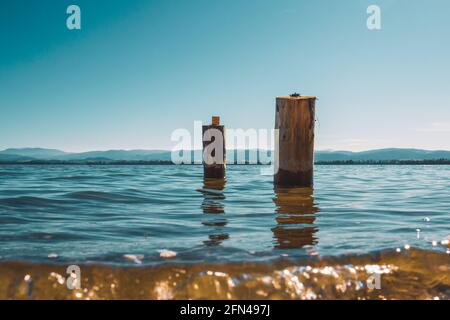 due pali di legno lavati dalle acque del lago con le montagne sullo sfondo Foto Stock