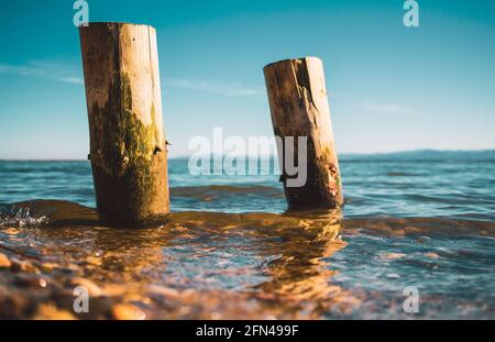 due pali di legno lavati dalle acque del lago con le montagne sullo sfondo Foto Stock