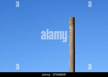 Un semplice palo di cemento. Un lungo palo sotto un cielo blu in una giornata di sole. Solitudine e minimalismo. Foto Stock