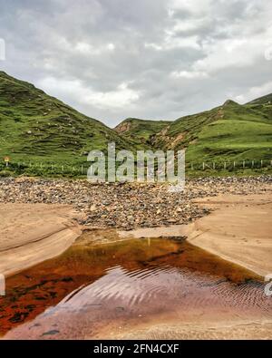 Strana spiaggia irlandese con acqua sporca e stagnante. Piccola spiaggia rocciosa in giorno nuvoloso. Foto Stock