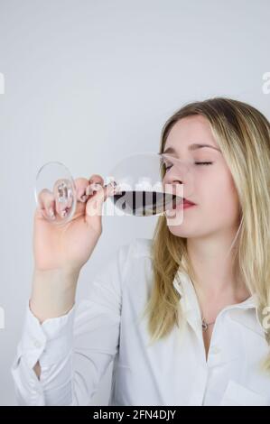 Ritratto di una bella giovane bionda che assaggia un rosso vino in calice in una degustazione di vini Foto Stock