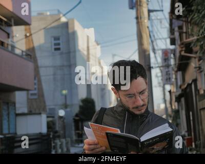 Un turista in giappone legge una guida di viaggio. Giovane turista con occhiali legge una guida di tokyo per orientarsi in città. Turismo vecchio stile. Foto Stock