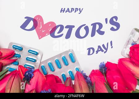 Fiori e pillole con iscrizione Happy Doctor's Day su bianco. Biglietto d'auguri. Foto Stock