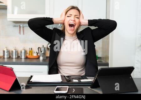 Disperata donna d'affari overwaged urla e grida in cucina. La donna tiene la testa nelle mani mentre soffre di una rottura nervosa. Foto Stock