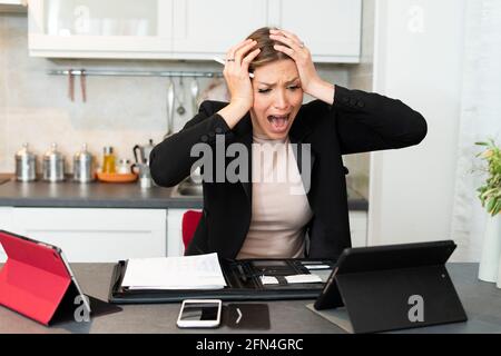 Disperata donna d'affari overwaged urla e grida in cucina. La donna tiene la testa nelle mani mentre soffre di una rottura nervosa. Foto Stock