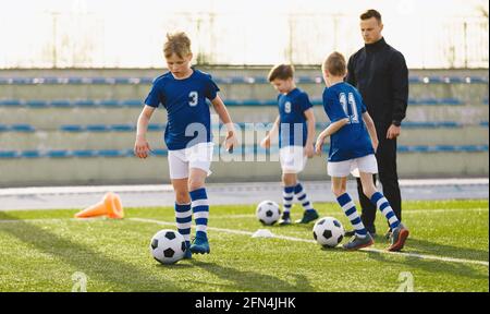 Ragazzi sportivi in blu che corrono e calciano una palla in campo. La squadra giovanile di calcio gioca l'allenamento di calcio in estate. Sport acti Foto Stock