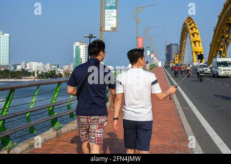 I turisti maschi che usano il bastone selfie camminando sopra il Ponte del Drago durante il giorno, da Nang, Vietnam Foto Stock