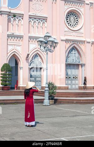 Attraente turista femminile con cappello conico e tradizionale abito vietnamita ao dai alla Cattedrale di da Nang (chiesa rosa), da Nang, Vietnam Foto Stock