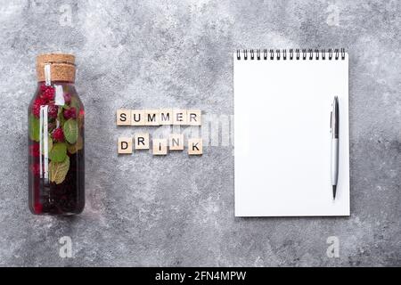Concetto di bevanda sana d'estate. Limonata di Berry in bottiglia di vetro con taccuino bianco e lettere di legno parola Summer drink su sfondo grigio di cemento Foto Stock