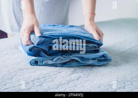 Donna piega un jeans sulla copertura grigia sul letto. Pila di vestiti blu jeans Foto Stock