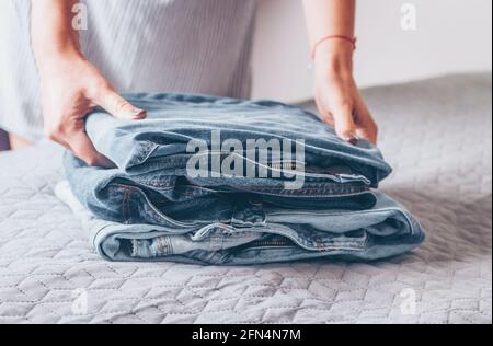 Donna piega un jeans sulla copertura grigia sul letto. Pila di vestiti blu jeans Foto Stock