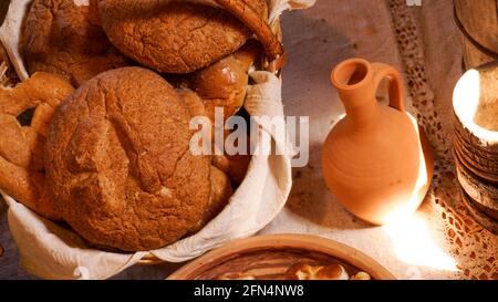 Pane fresco fatto in casa in un cestino su un tavolo di legno. Creta pentole accanto al cesto. Stile rustico Foto Stock